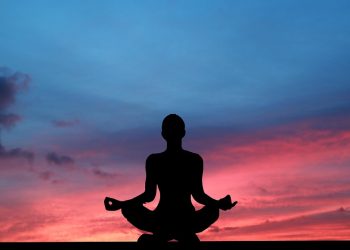 Silhouette meditating at sunset with vibrant sky.