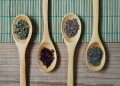 Wooden spoons with assorted spices on a bamboo mat.