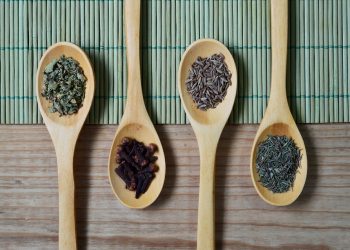 Wooden spoons with assorted spices on a bamboo mat.