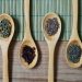 Wooden spoons with assorted spices on a bamboo mat.