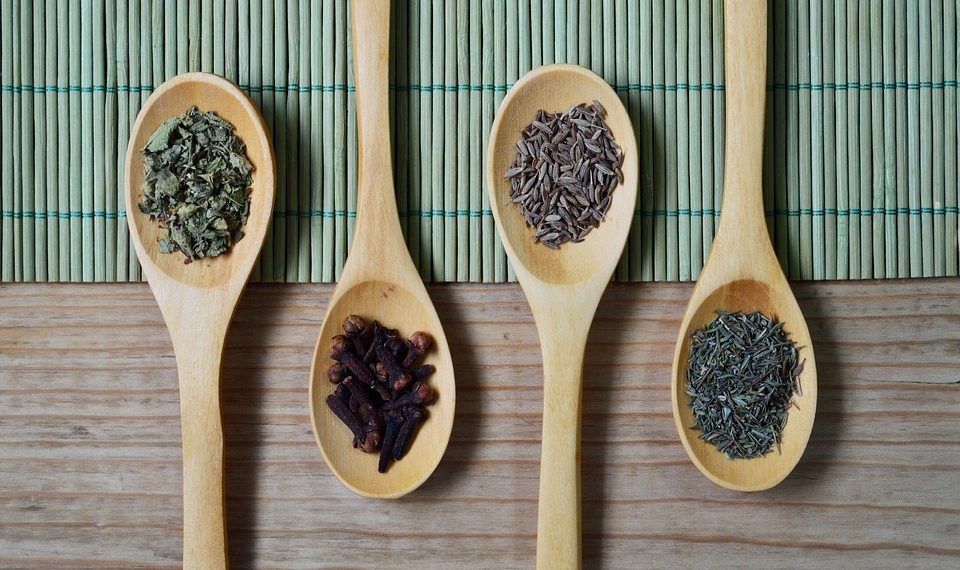 Wooden spoons with assorted spices on a bamboo mat.