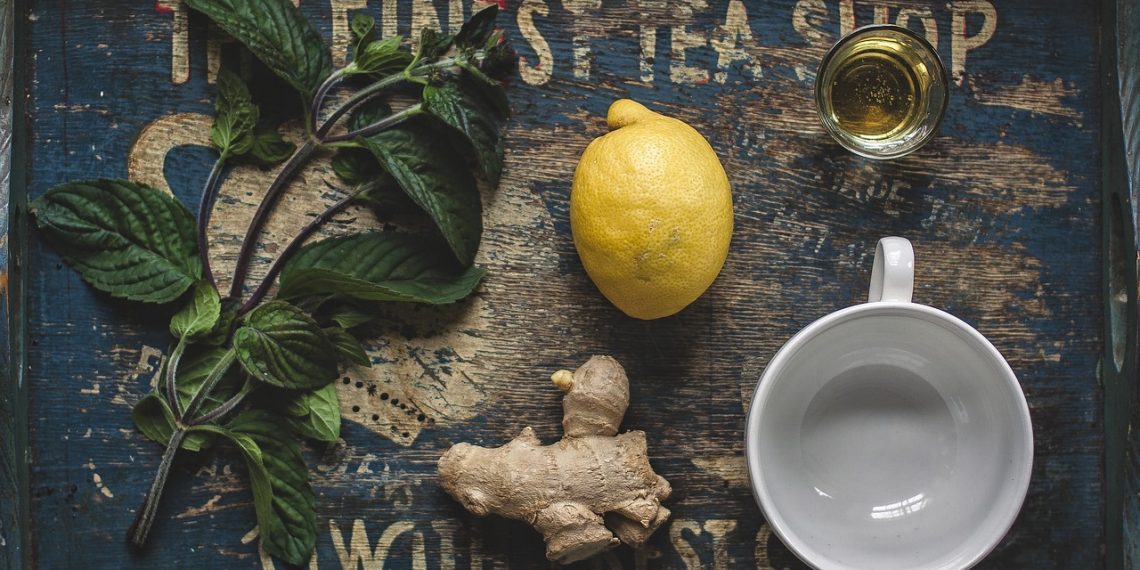 Fresh mint, lemon, and ginger with tea cup on rustic tray.