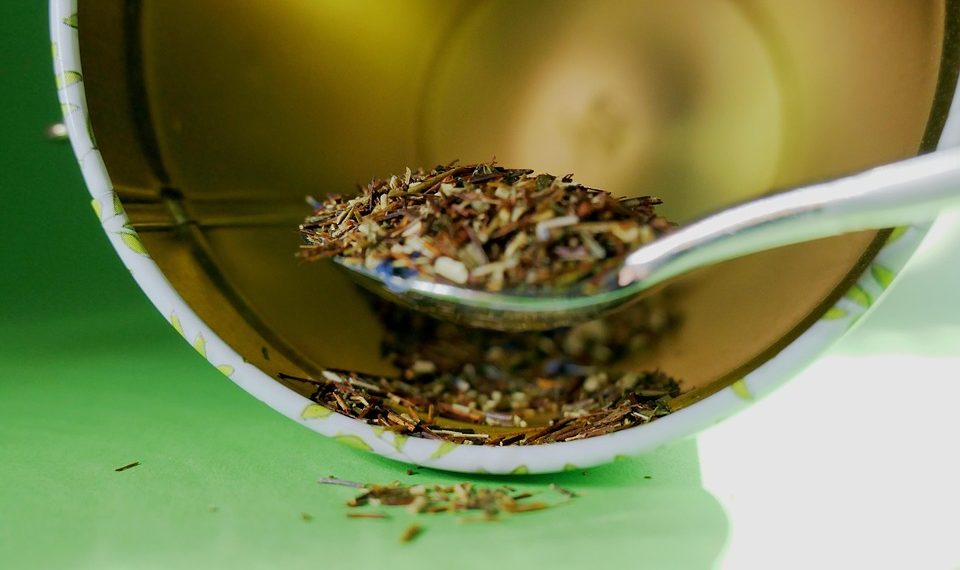 Spoon scooping fresh loose leaf tea into cup.