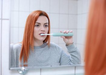 Woman brushing teeth with an electric toothbrush in front of a mirror.