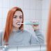 Woman brushing teeth with an electric toothbrush in front of a mirror.