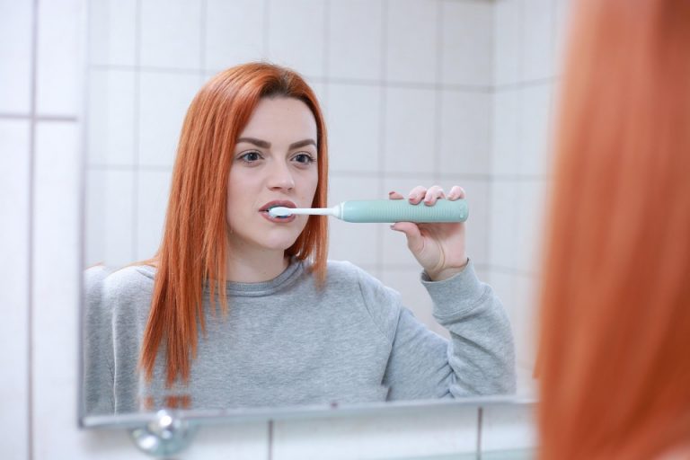 Woman brushing teeth with an electric toothbrush in front of a mirror.