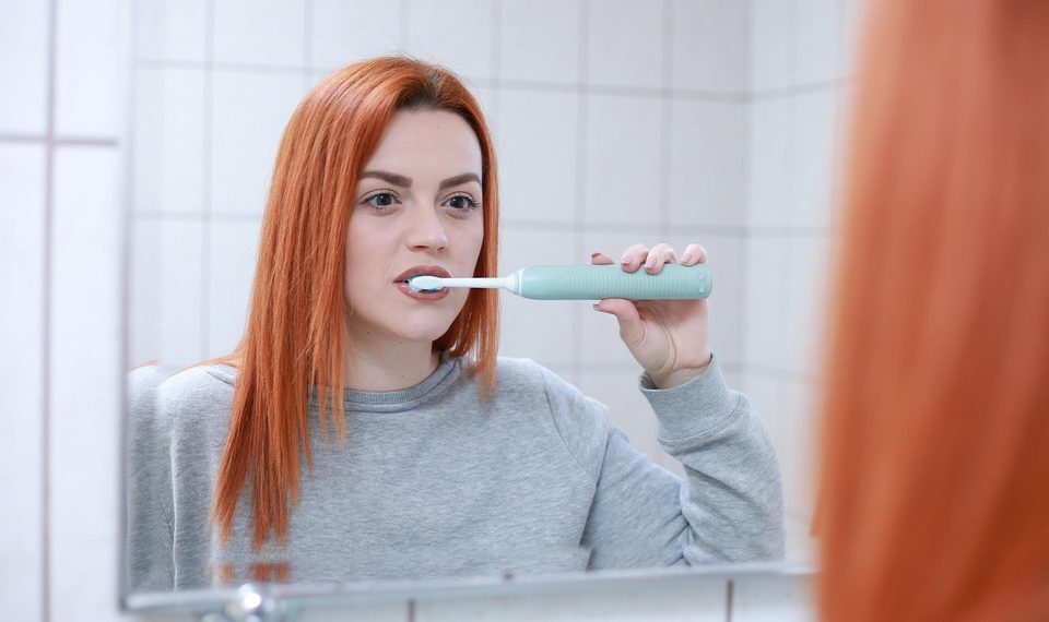 Woman brushing teeth with an electric toothbrush in front of a mirror.