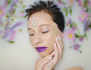 Woman with floral decorations relaxing in milk bath.