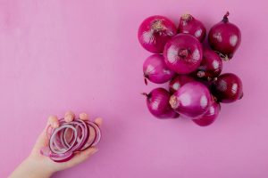 Hand holding sliced red onion rings next to whole onions.