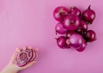 Hand holding sliced red onion rings next to whole onions.