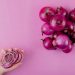 Hand holding sliced red onion rings next to whole onions.