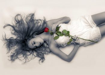 Lying woman with a flowy dress holding a single red rose.