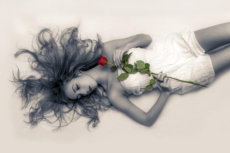Lying woman with a flowy dress holding a single red rose.