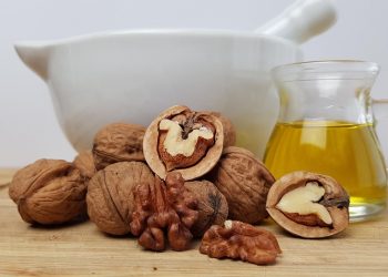 Walnuts with oil and mortar on wooden surface.