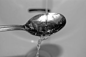 Water pouring onto a spoon in a sink basin.