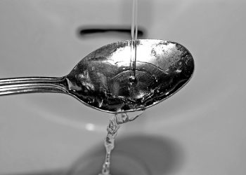 Water pouring onto a spoon in a sink basin.