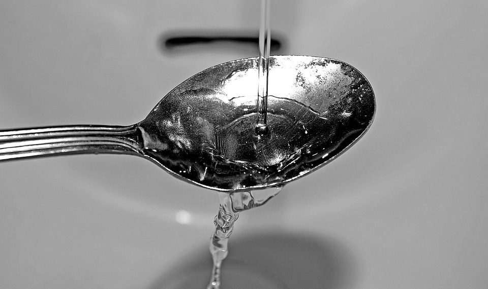 Water pouring onto a spoon in a sink basin.