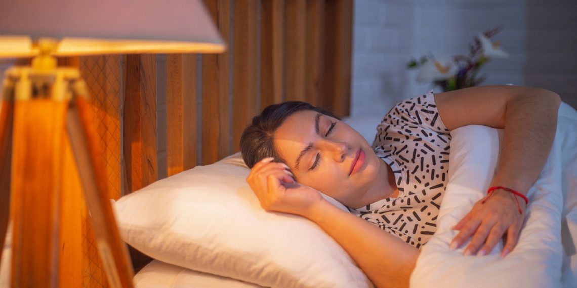 Sleeping woman in comfortable bed under soft lighting.