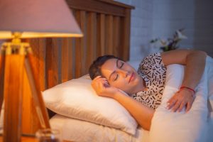 Sleeping woman in comfortable bed under soft lighting.