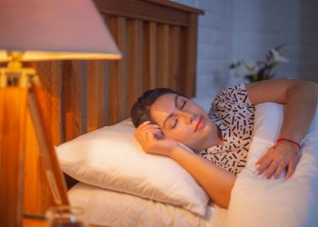 Sleeping woman in comfortable bed under soft lighting.