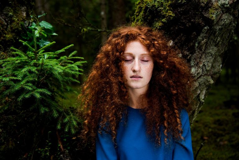 Young woman with closed eyes in a forest setting, surrounded by lush greenery.