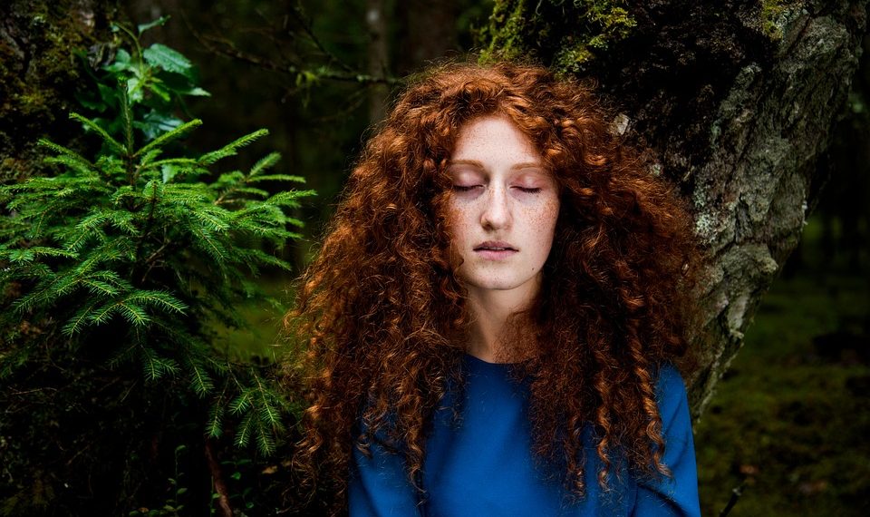 Young woman with closed eyes in a forest setting, surrounded by lush greenery.