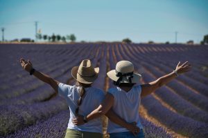 Two women in hats embrace, enjoying a lavender field vista.