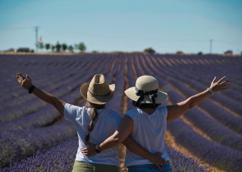 Two women in hats embrace, enjoying a lavender field vista.