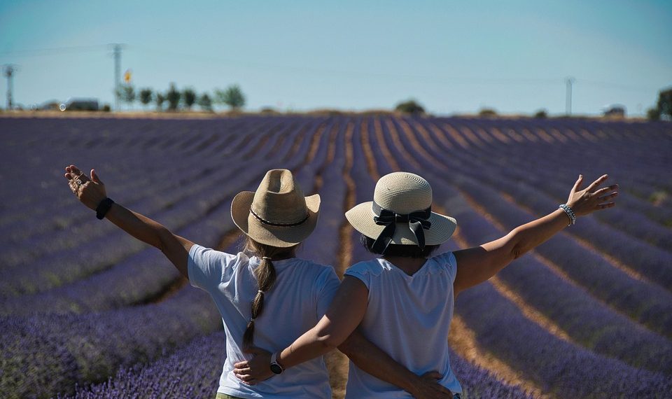 Two women in hats embrace, enjoying a lavender field vista.