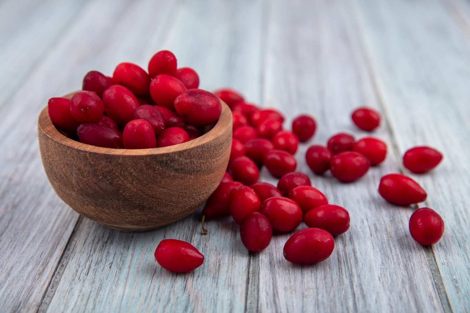 Side view of cornel berries in bowl and on wooden background berberine