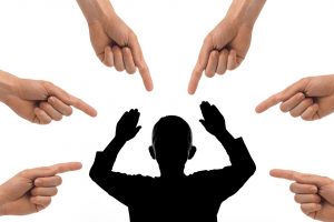 Silhouette of a person surrounded by pointing hands, symbolizing blame.