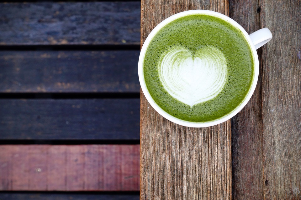 A cup of green tea with a heart shape in the center, symbolizing healthy aging and antioxidants in a flat lay arrangement.