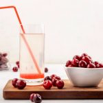 Side view of cherry juice with drinking tube in glass and cherries in bowl