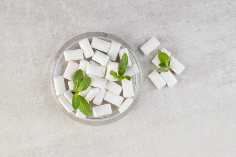 Top view of pile of gums with mint leaves in glass bowl.