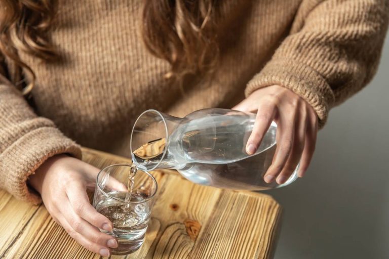 A woman pours water into a glass from a glass decanter