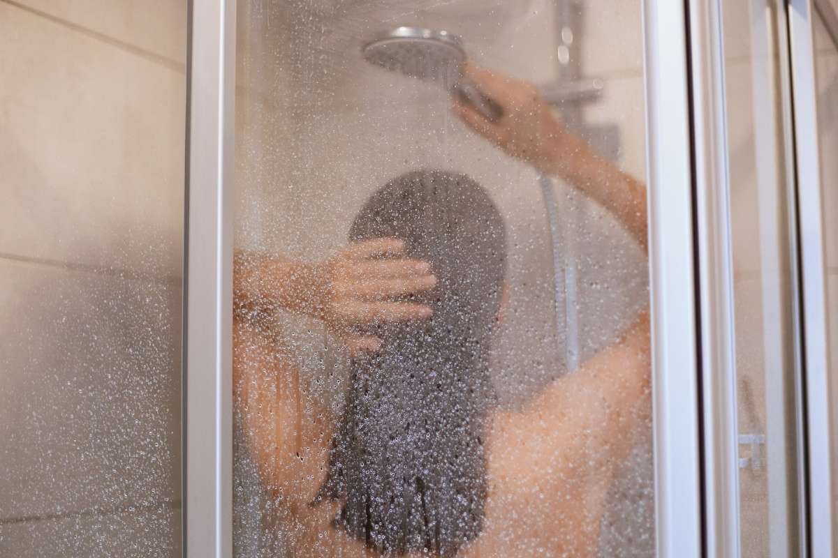 Enjoying a shower. Back view of beautiful young slim shirtless woman taking sh