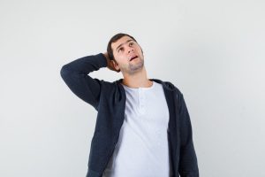 Young man in white t-shirt and zip-front black hoodie putting hand behind head,thinking about something