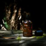 Aesop product bottle sits on wood in dim light.