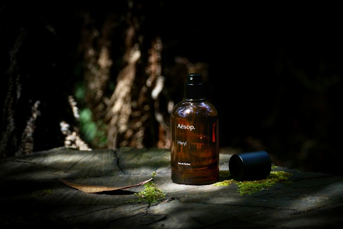 Aesop product bottle sits on wood in dim light.