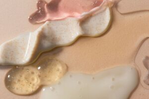 Swirls of pink gel, white exfoliating cream, and clear serum on a beige surface