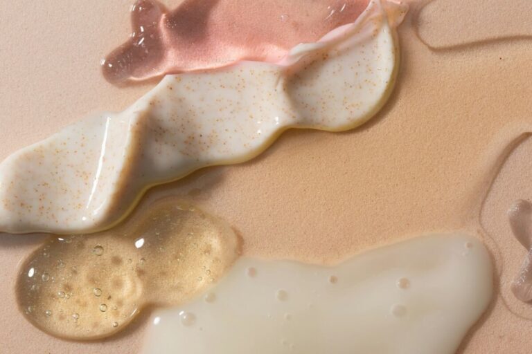 Swirls of pink gel, white exfoliating cream, and clear serum on a beige surface