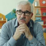 Elderly man with glasses resting chin on hands