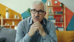 Elderly man with glasses resting chin on hands