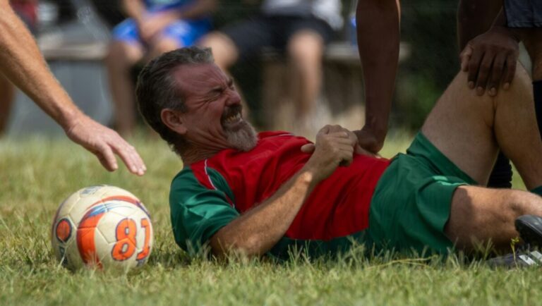 Man in soccer uniform grimacing on grass
